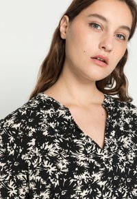 Blusa de padrão floral em preto e creme, com decote em V e mangas curtas, feita de um tecido leve e texturizado.