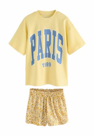 T-shirt di cotone gialla con stampa blu "PARIS 1989", abbinata a pantaloni corti a fantasia floreale gialli e bianchi, dotati di vita elastica.