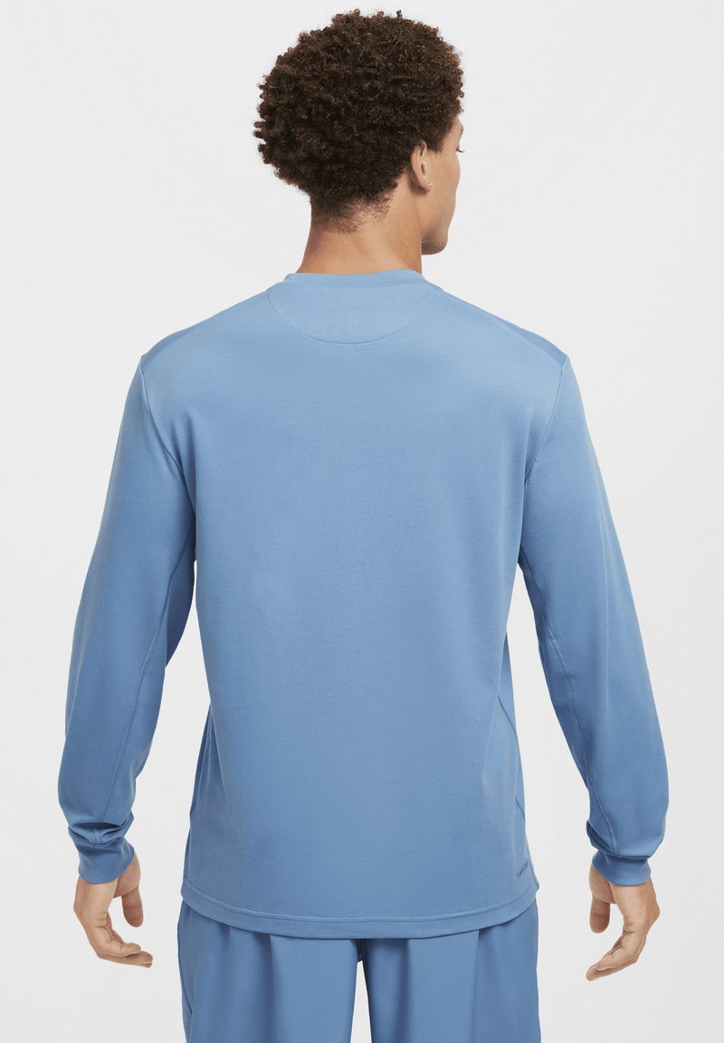 Jasnoniebieska koszula z długim rękawem, wykonana z miękkiego materiału, z okrągłym dekoltem i bezszwowym wykończeniem ramion. Tył jest gładki, bez wyraźnych detali.