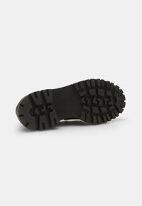 Black rubber outsole with deep treads and sturdy design. Textured surface features patterns for enhanced grip.