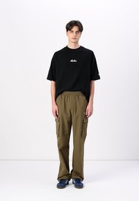 Black short-sleeve t-shirt with white logo, paired with olive cargo pants featuring pockets, and blue sneakers with black accents.