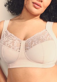 Sutien din material bej deschis, cu un panou de dantelă în partea de sus și bretele reglabile. Textură netedă, design cu acoperire completă pentru suport.