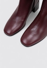 Bottines en cuir bordeaux avec un bout carré, texture lisse et un talon bloc. Équipées d'une fermeture éclair sur le côté pour un enfilage facile.