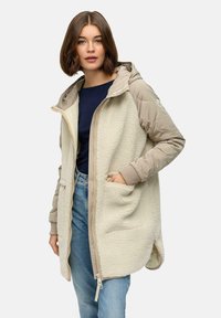 Fleece-foret jakke med en cremet krop og beige quiltede ærmer, hætte og lommer. Har en frontlynlås og sidelængder for nem bevægelse.