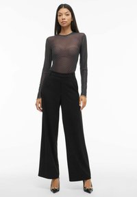 Czarny, przezroczysty, długi rękaw, body w kropki, zestawione z czarnymi, szerokimi spodniami z wysokim stanem oraz czarnymi szpilkami z szpiczastym noskiem.