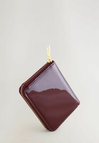 Portafoglio zip bordeaux in pelle lucida con hardware in tonalità oro e cuciture a contrasto. Forma quadrata e texture liscia, con chiusura a zip.