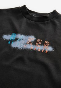 Melnā kokvilnas sporta krekls ar grafisku dizainu, uz kura ir uzraksts "BAKER" zilā un oranžā krāsā, un apakšā teksts "by TED BAKER" ar teksturētu apdari.