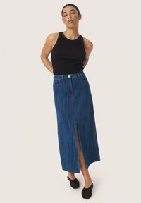 Temna jeans maxi krilna z sprednjim razporkom, visokim pasom in petimi žepi, v kombinaciji z oprijetim črnim brezrokavnikom in črnimi čevlji.