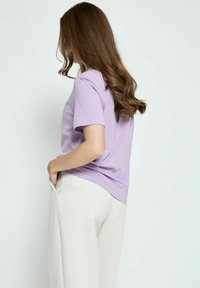 Šviesiai violetinė trumpomis rankovėmis marškinėliai iš lengvos medžiagos, su laisvu siluetu ir apvaliu iškirpimu, derinami su kreminės spalvos plačiomis kelnėmis.