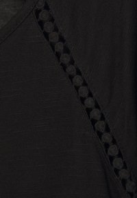 Top nero realizzato in un materiale testurizzato con un bordo in pizzo decorativo lungo una spalla, che aggiunge un dettaglio a contrasto sottile.