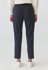 Tmavě modré kalhoty s elastickým pasem, dvěma zadními kapsami a slim fit střihem. Vyrobeny z hladké tkaniny s tapered nohou.