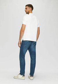Weißes Poloshirt mit kurzen Ärmeln, blaue Denim-Jeans und weiße Sneakers. Das Poloshirt hat einen klassischen Kragen, und die Jeans sind mit Gesäßtaschen ausgestattet.