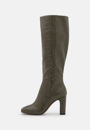 Botte haute jusqu'au genou de couleur vert olive avec texture crocodile et talon haut épais, vue de côté sur fond blanc.