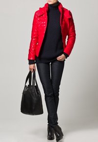 Röd, glansig puffjacka med dragkedja och huva, bärs över en marinblå polotröja, ihop med mörka jeans och en svart läderväska, accentuerat med ankle boots.