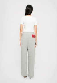 Grå sweatpants med en løs pasform, elastisk talje, og rød label detalje bagpå, parret med en tætsiddende hvid T-shirt.