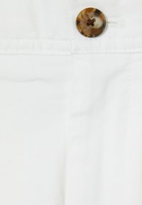 Țesătură albă cu o textură fină, având un buton rotund, multicolor, în partea de sus și cusături curate pe margini.