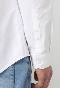 Wit overhemd met lange mouwen, voorzien van een ronde zoom en manchetten met één knoop, gecombineerd met lichtblauwe denim jeans.