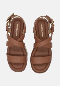 Sandali in pelle marrone con fasce incrociate, fibbia regolabile alla caviglia e soletta leggermente imbottita. Logo dorato "Michael Kors" stampato.