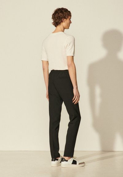 Zwarte elastische taille broek gecombineerd met een crèmekleurige gebreide top met korte mouwen en witte sneakers met zwarte accenten. Soepele textuur, eenvoudige silhouet.