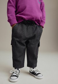 Lila Sweatshirt, graue gemusterte Hose mit Seitentaschen und schwarze Sneaker mit weißen Schnürsenkeln; lässiger Look mit entspannter Passform.
