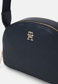 Borsa a tracolla in pelle blu navy con forma arrotondata, zip dorata e accento in metallo a logo. Texture liscia con tracolla sottile e regolabile.