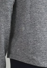 Harmaa kirjavilla pitkähihaisen puseron, joka on valmistettu teksturoidusta kankaasta. Puserossa on huomaamaton logo sivussa sekä rento istuvuus, jossa on pyöristetty helma.