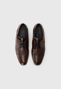 Zapatos de vestir de cuero marrón con una textura suave, forma de punta afilada y detalles de costura mínimos. Presentan cordones oscuros y plantillas con marca.