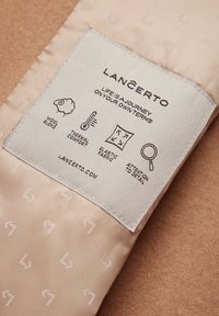 Beżowa metka z składem z mieszanki wełny, zawierająca ikony dotyczące komfortu termicznego, elastycznego materiału oraz dbałości o szczegóły, z wyświetlonym logo.