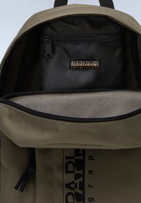 Innenraum eines olivgrünen Rucksacks mit einer schwarzen Reißverschlusstasche. Langlebiges Material, graue Innenauskleidung und Markenlogo auf der Innenseite.