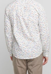 Camisa de manga larga floral en blanco, con un patrón de pequeñas flores multicolores. Tejido suave con un dobladillo curvado y puños abotonados.