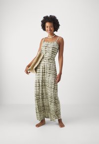 Maxi dress in green and white tie-dye pattern, made from lightweight fabric, with adjustable straps and a drawstring waist. Accompanied by a textured bag.