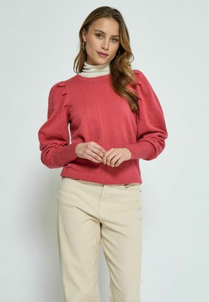 Korallenrosa gestrickter Pullover mit puffigen Ärmeln und gerippten Bündchen, kombiniert mit beigen Hosen, zeichnet sich durch subtile Textur und einen runden Ausschnitt aus.