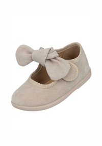 Zapato de tela color beige con punta redonda, textura suave y un gran lazo decorativo en la parte delantera. Cuenta con una cinta elástica para un ajuste seguro.