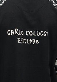 Μαύρο ένδυμα με λευκό κεντημένο κείμενο "CARLO COLUCCI EST. 1978" και μαύρο-λευκό υφασμάτινο μοτίβο στους ώμους.