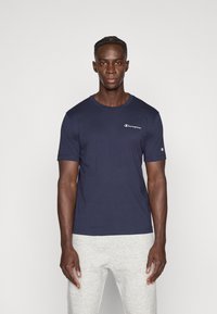 Μπλε ναυτικό βαμβακερό μπλουζάκι με στρογγυλή λαιμόκοψη, κοντά μανίκια και λευκό λογότυπο Champion στο στήθος. Απαλή υφή και κλασική εφαρμογή.