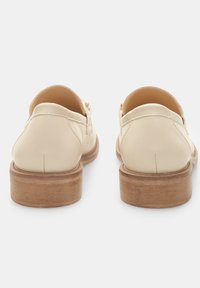 Scarpe in pelle crema con tacco in legno basso, caratterizzate da un retro arrotondato e da un dettaglio di cucitura sottile lungo le cuciture.