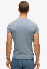 T-shirt bleu chiné à manches courtes avec un col rond, silhouette ajustée et texture lisse semblable au coton, associé à un jean en denim.