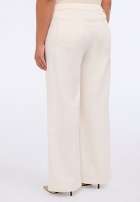 Pantaloni ampi crema con cintura elastica, due tasche posteriori e texture liscia, abbinati a tacchi a punta.