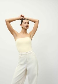 Gaiši dzeltens bezramen tops, pieskaņots augsto jostasvietu off-white biksēm ar gludu tekstūru un minimālistisku dizainu.