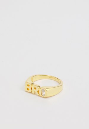 Goldfarbener Ring mit Blockbuchstaben "BRO" und einem klaren ovalen Steinakzent, glattem Design des Bands und polierter Oberfläche.