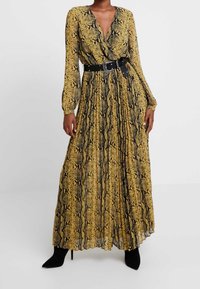 Robe longue imprimé serpent jaune et noir avec manches longues, col en V profond et ceinture noire à la taille. Tissu texturé avec des plis.
