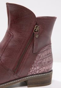 Bottine bordeaux avec fermeture éclair latérale, talon texturé à motif crocodile et talon bas empilé en bois.