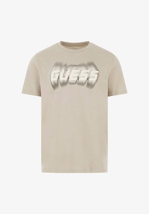 Világos bézs pamut póló, fehér és szürke elmosódott "GUESS" logóval. Rövid ujjú és kerek nyakú.