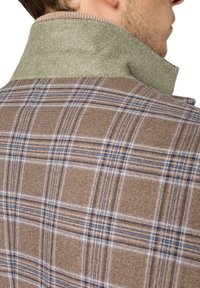 Brązowa i beżowa marynarka w kratę z zielonym filcowym kołnierzem. Wzór zawiera niebieskie linie. Tekstura wydaje się tkana i ciepła.