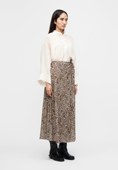 Λευκό, ελαφρώς διάφανο πουκάμισο με κουμπιά και μακριά μανίκια· μακρύ φούστα με μοτίβο λεοπάρ και κόμπο στο πλάι· μαύρα μποτάκια έως τον αστράγαλο.