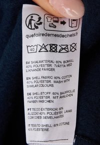 Kledinglabel met verzorgingsinstructies, gedrukt in meerdere talen. Stofsamenstelling: 60% katoen, 40% polyester. Inclusief wassymbolen.
