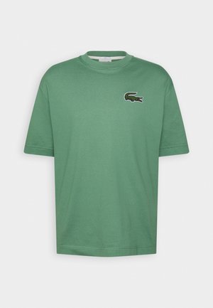 Groen T-shirt met korte mouwen en ronde hals, met klein geborduurd krokodillenlogo op de linkerborst tegen een effen achtergrond.