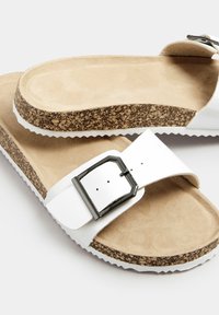 Sandali da donna bianchi con suola in sughero, texture scamosciata, cinturino regolabile con fibbia metallica e suola in gomma bianca.