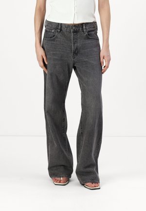 Person iført højtaljede, falmede sorte vidde jeans kombineret med hvide sandaler med firkantet tå og en hvid ærmeløs cropped top.