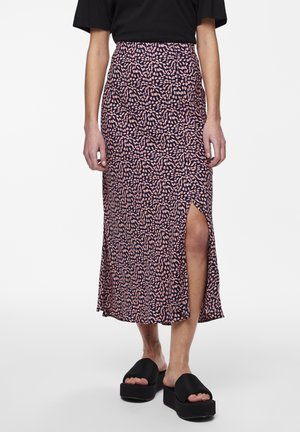 Vrouw met een zwarte top en een midi-rok met patroon en een zijsplit, gecombineerd met zwarte platform schuifzandalen.